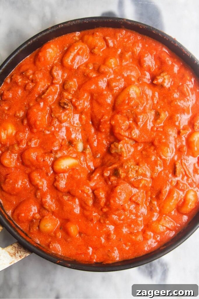 Creamy One-Pot Sausage Gnocchi Delight 8 The gnocchi are carefully stirred through the creamy tomato sauce, ensuring each piece is fully coated and ready to cook perfectly.