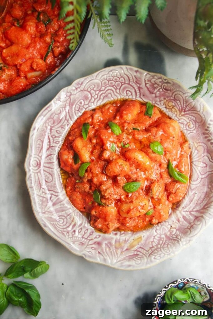 Creamy One-Pot Sausage Gnocchi Delight 10 A beautifully plated dish of creamy tomato sausage gnocchi, garnished with fresh basil leaves, resting on a pink plate.