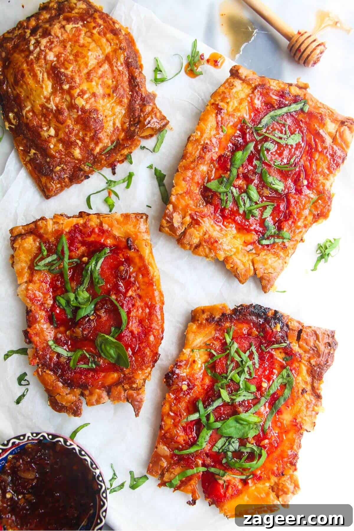 Puff Pastry Pizza Flips 2 Four golden-brown upside down puff pastry pizza tarts neatly arranged on baking paper, with a small bowl of vibrant sweet chilli jam alongside, ready for serving.