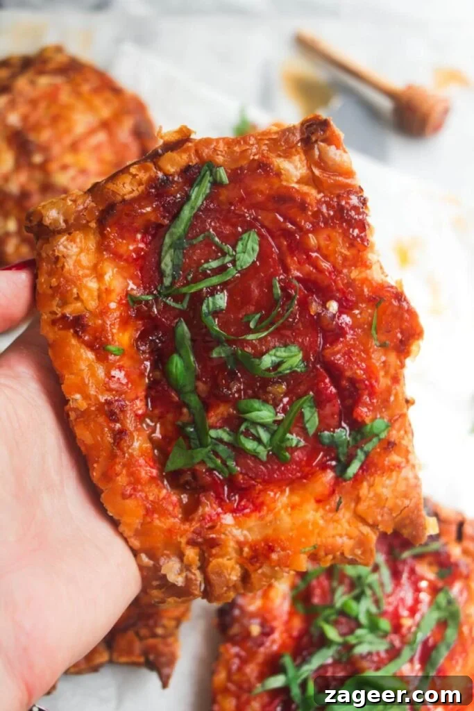 Puff Pastry Pizza Flips 11 A hand confidently holding up a perfectly baked upside down puff pastry pizza tart, displaying its enticing layers and golden crust.