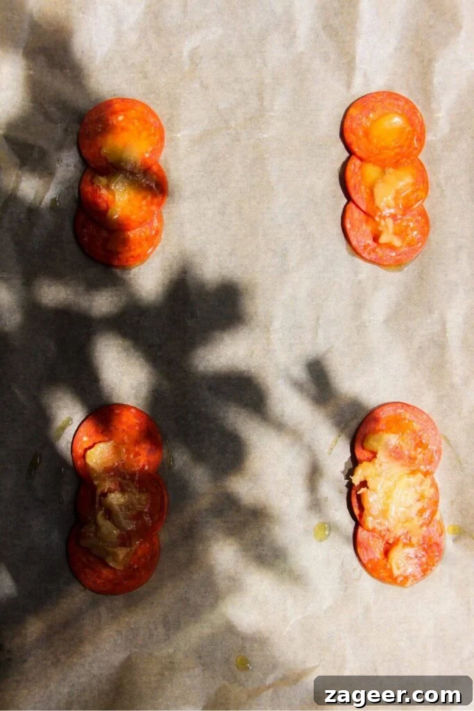 Puff Pastry Pizza Flips 4 Confit garlic cloves delicately placed atop vibrant pepperoni slices on a lined baking tray, forming the savory base of the upside-down tarts.