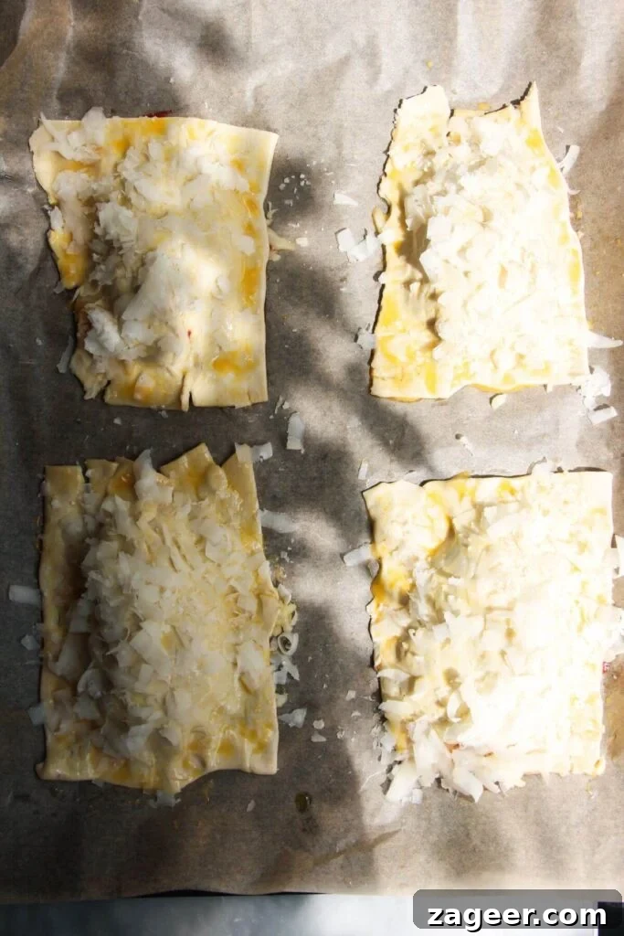 Puff Pastry Pizza Flips 7 Parmesan-topped puff pastry rectangles delicately placed over the pizza filling on a lined baking tray, ready for baking and transformation.