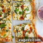 Golden Zucchini Puff Pastry Tart 10 Zucchini puff pastry tart sliced, with a hand pulling one piece out.