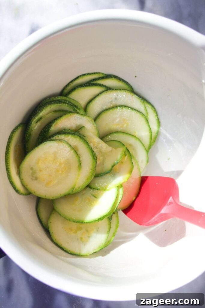 Golden Zucchini Puff Pastry Tart 4 Thinly sliced zucchini, perfectly seasoned with olive oil and salt, in a white mixing bowl, ready for layering.