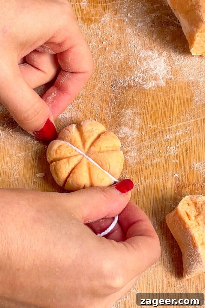 Effortless 5-Ingredient Sweet Potato Gnocchi 14 Hands holding string, pressing down on gnocchi dough to create a pumpkin shape.