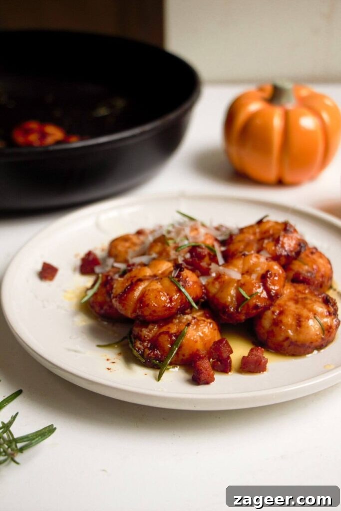 Effortless 5-Ingredient Sweet Potato Gnocchi 15 Close up of pumpkin shaped sweet potato gnocchi on a small white plate with a gold spoon.