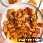 Hand holding a plate of sweet potato gnocchi with a gold spoon in it.