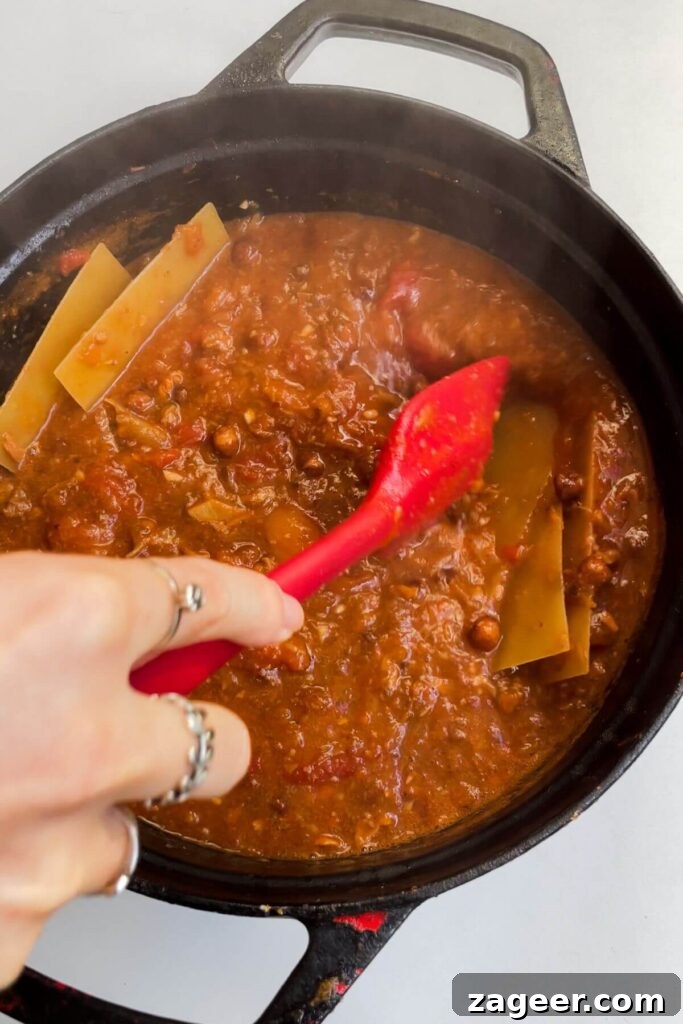 Stealthy Veggie One Pot Lasagna Soup 8 Hand holding spatula, stirring lasagna sheets through soup in a large pot to prevent sticking.