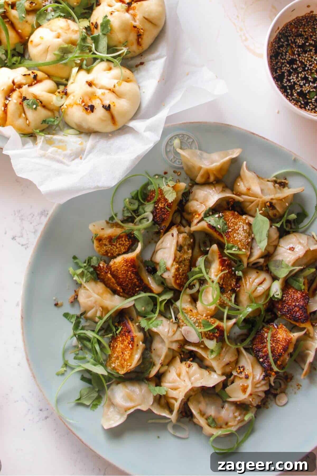 Chicken potstickers on a large blue plate with sauce and steamed buns on the side.