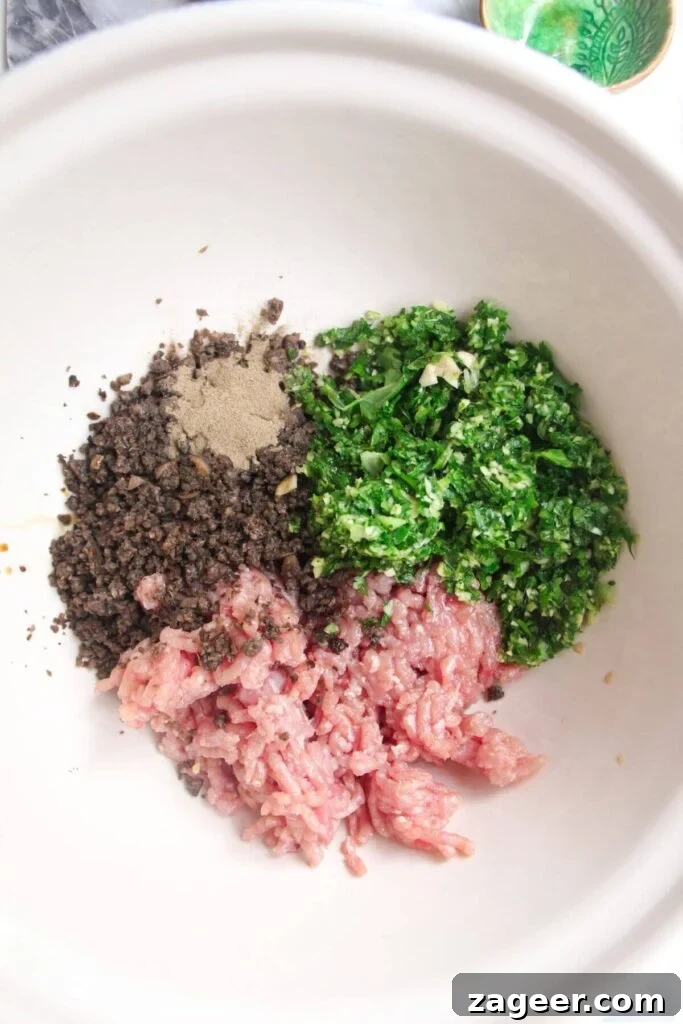 Ground chicken, herbs, mushrooms and seasoning in a large white mixing bowl.