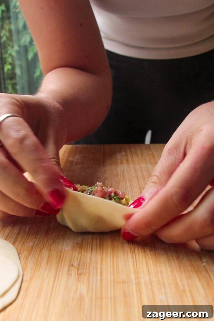 Hands folding dumpling on a wooden board.