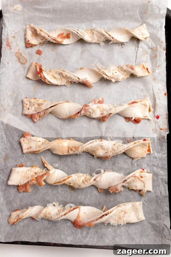 Numerous unbaked bacon cheese twists neatly arranged on a lined oven tray, ready for baking.