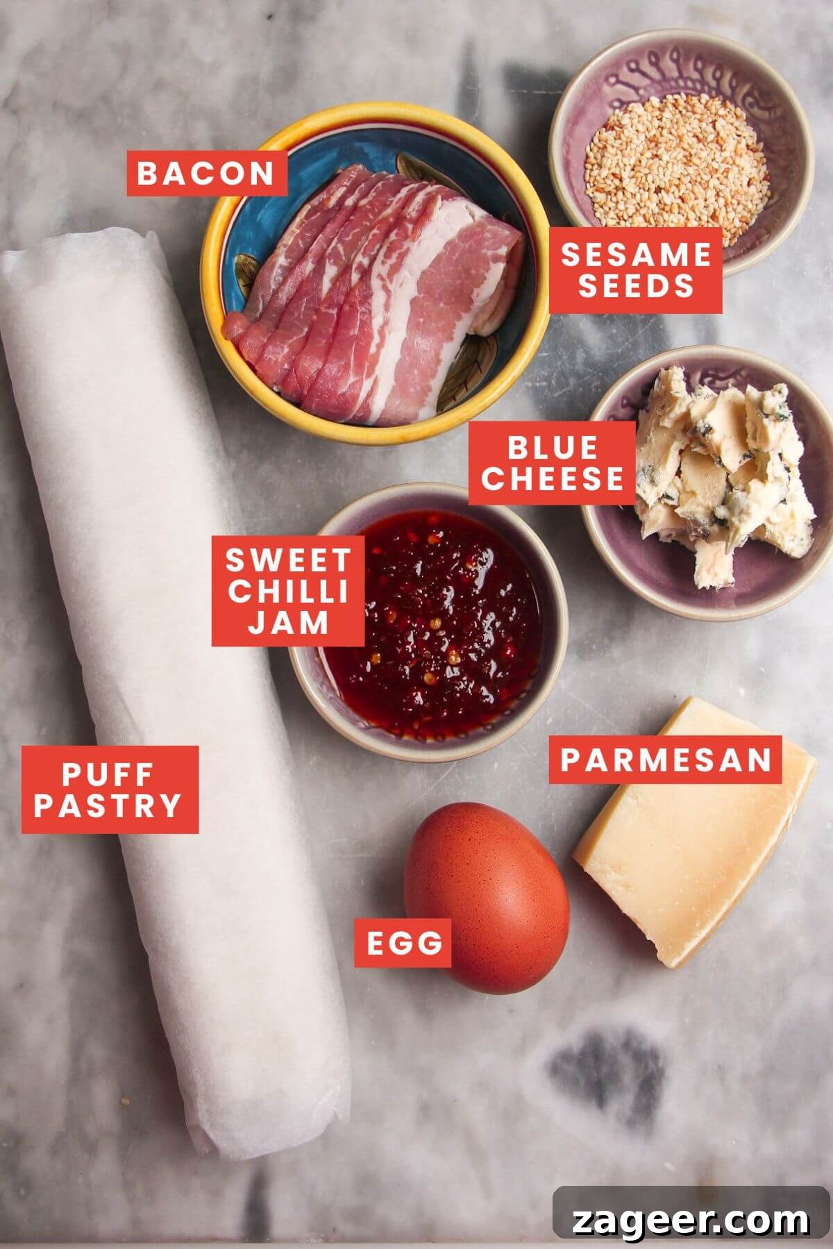Arrangement of ingredients for bacon blue cheese straws: puff pastry, streaky bacon, blue cheese, sweet chilli jam, parmesan, and sesame seeds.