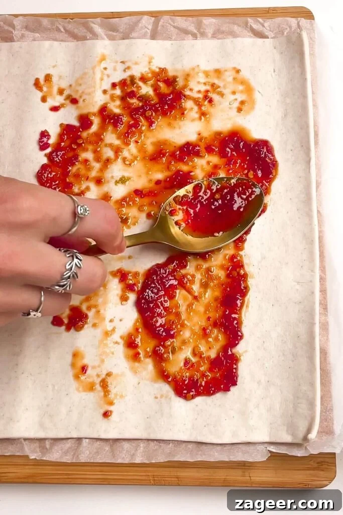 Spooning sweet chilli jam onto a sheet of puff pastry, spreading it evenly across one half.