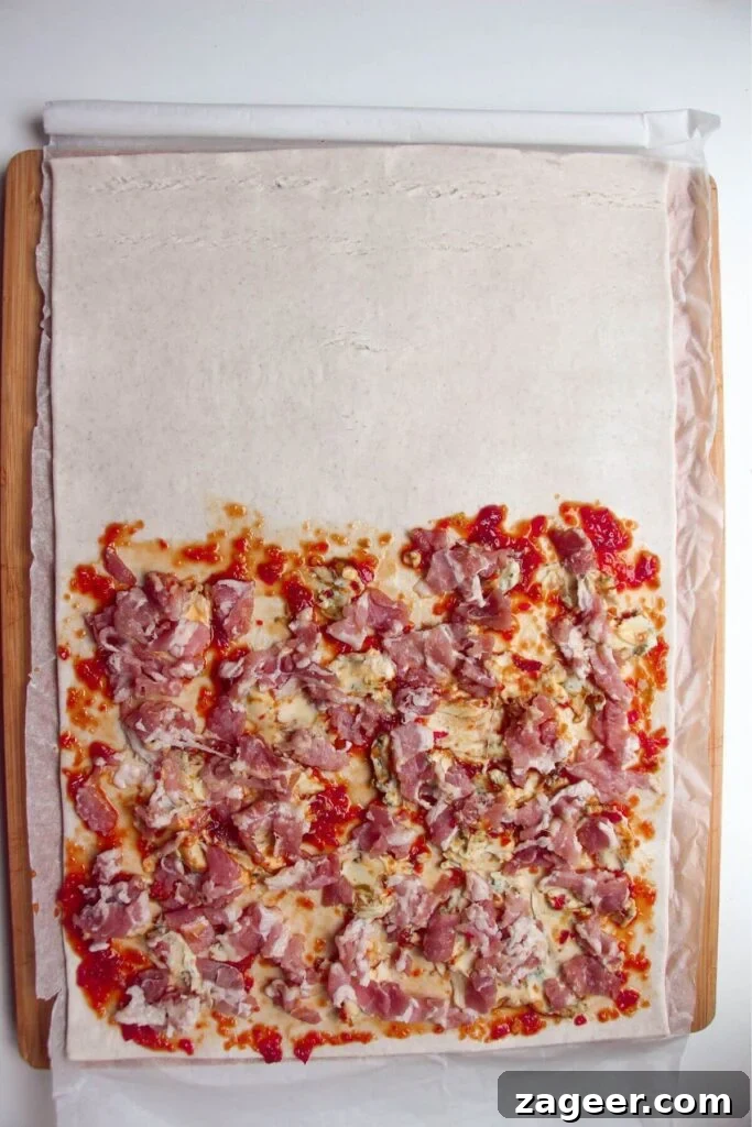 Chopped bacon, blue cheese, and sweet chilli jam evenly spread on one half of puff pastry.