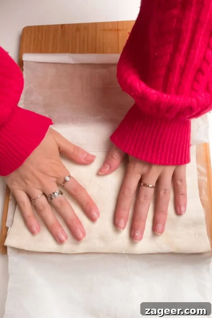 Hands carefully folding over the other half of puff pastry to cover the filling on a wooden board.