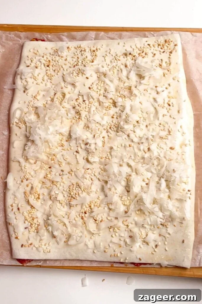 Grated parmesan cheese and sesame seeds sprinkled generously on top of egg-washed puff pastry.