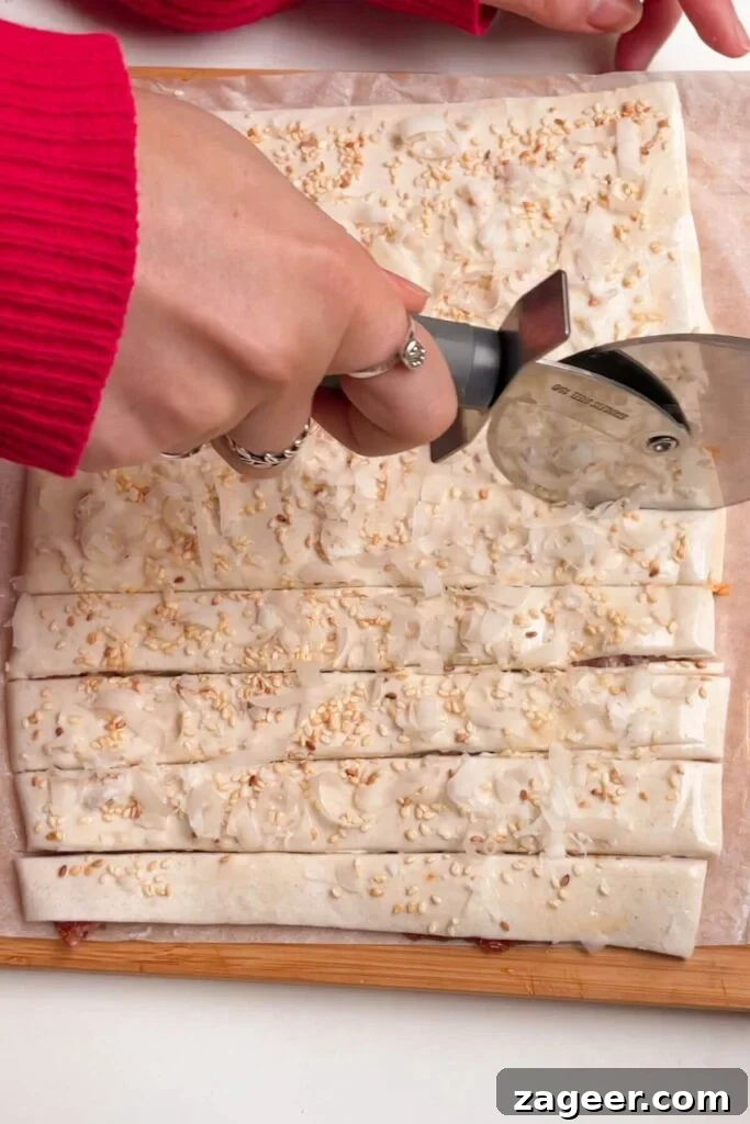 A hand holding a pizza cutter, expertly slicing through the puff pastry to create even strips.