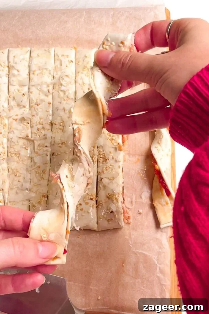 A hand gently holding an unbaked bacon blue cheese pastry twist, showcasing its spiral shape.