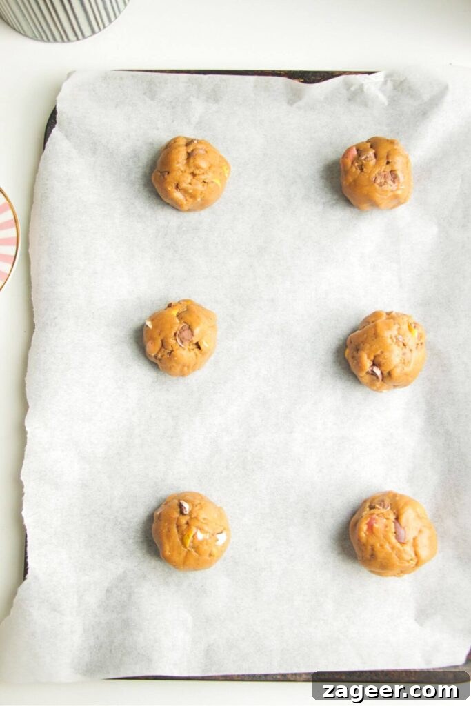 Six perfectly rounded cookie dough balls arranged on a baking paper lined oven tray, ready for the oven.