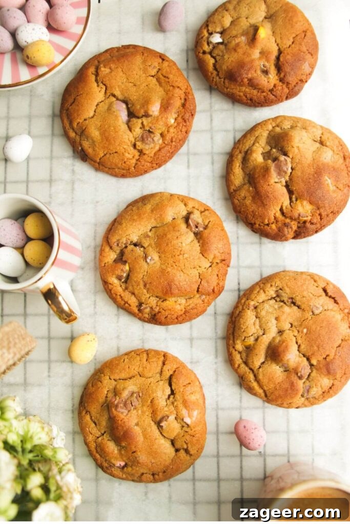A close-up shot of baked mini egg cookies on baking paper, with a generous scattering of whole mini eggs for decoration and context.