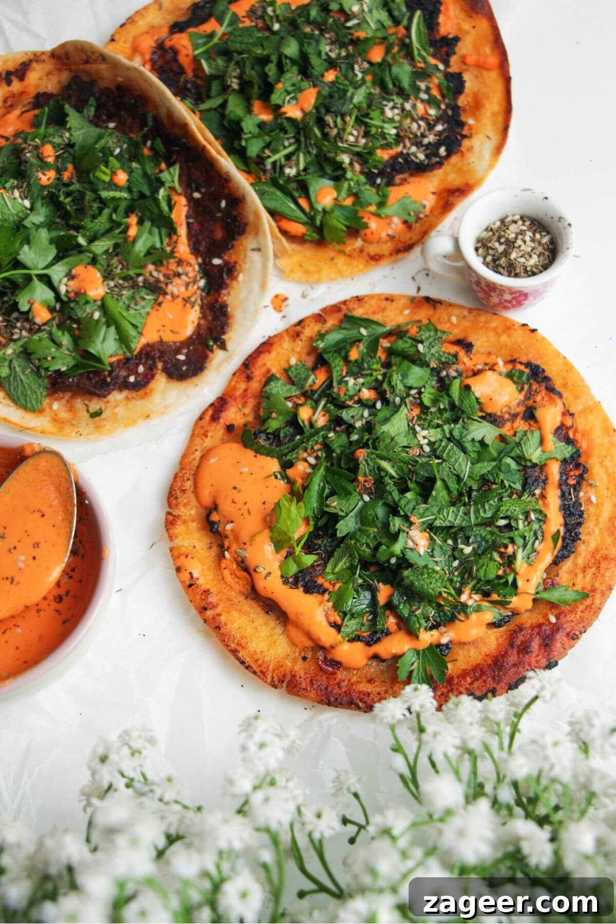 Effortless Lahmacun Smash Tacos 2 A vibrant Lahmacun Smash Taco, generously topped with smoky red pepper sauce and a refreshing herby salad, served on a light background.
