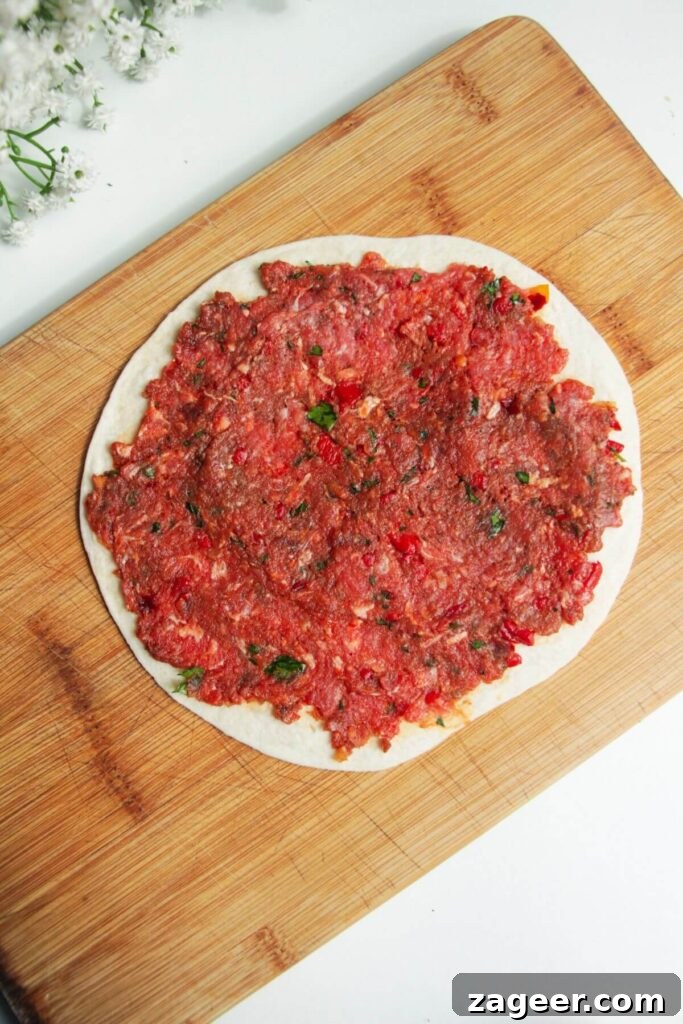 Effortless Lahmacun Smash Tacos 6 Lahmacun meat mixture thinly and evenly spread onto a mini tortilla, resting on a wooden board, poised for cooking.