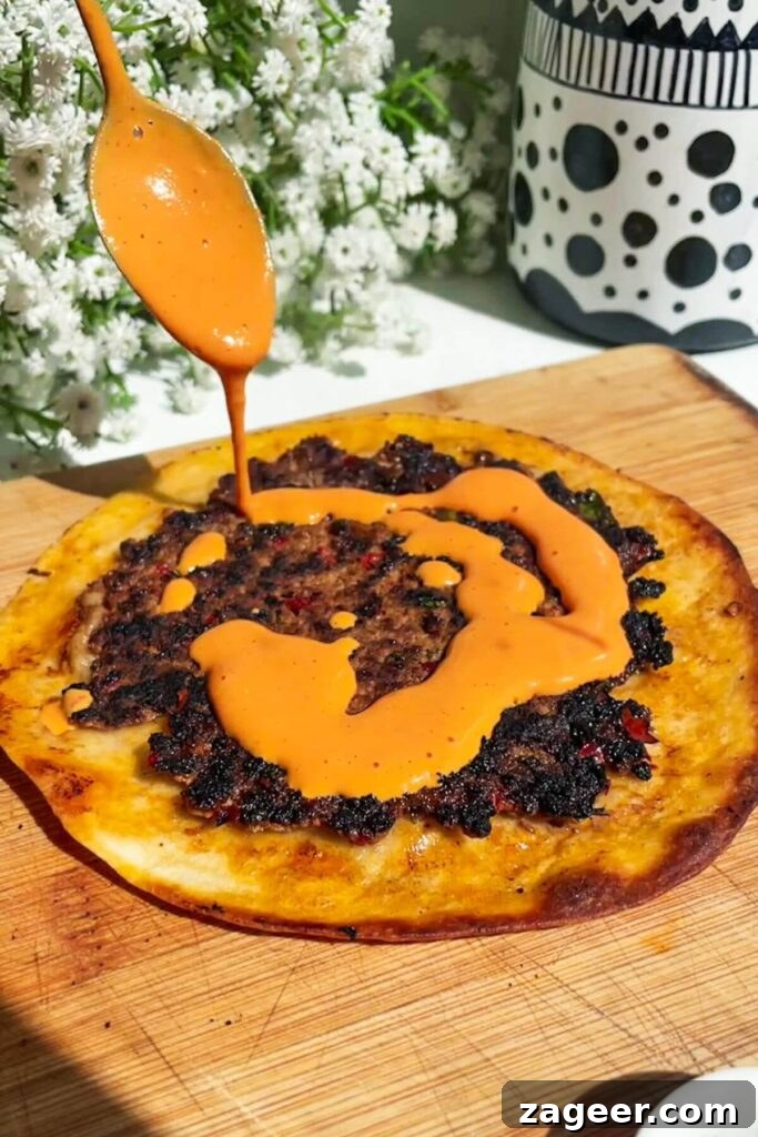 Effortless Lahmacun Smash Tacos 8 Drizzling the vibrant and creamy red pepper sauce generously on top of a freshly cooked smash lahmacun taco.