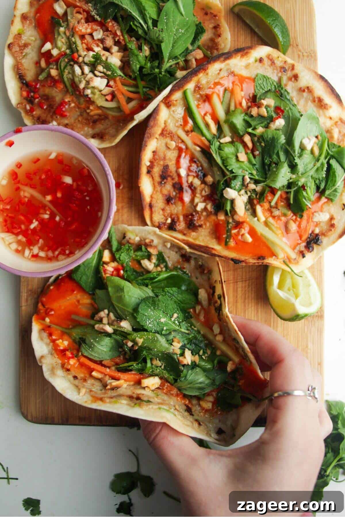Smashed Banh Mi Tacos 2 Three chicken banh mi tacos on a wooden board, garnished with fresh herbs and pickled vegetables.