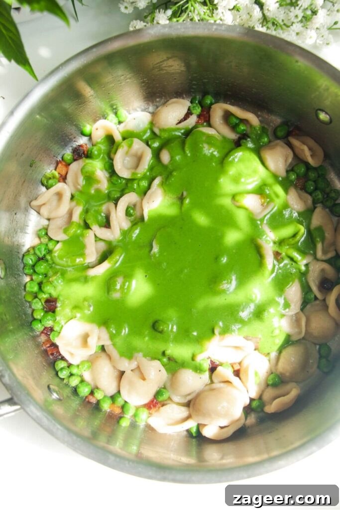 Silky Pancetta, Pea, and Spinach Pasta 9 The vibrant green spinach and basil sauce being poured over the cooked pasta, peas, and pancetta in a pan, ready for tossing.