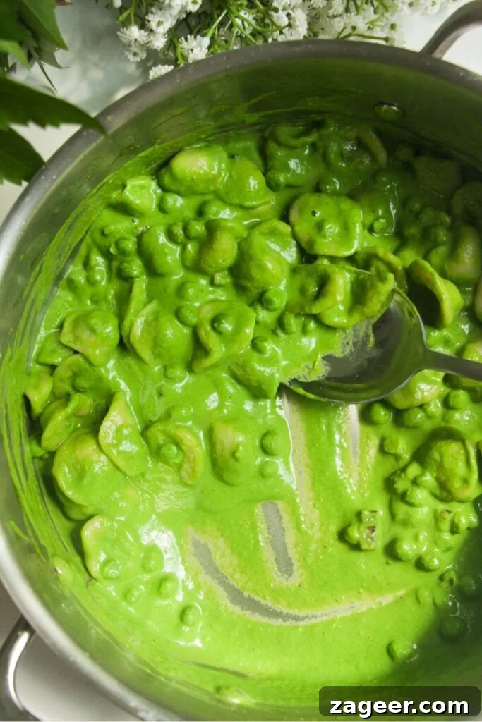 Silky Pancetta, Pea, and Spinach Pasta 10 The creamy spinach and basil sauce being thoroughly mixed through the peas, pancetta, and pasta in a pan, creating a vibrant and cohesive dish.