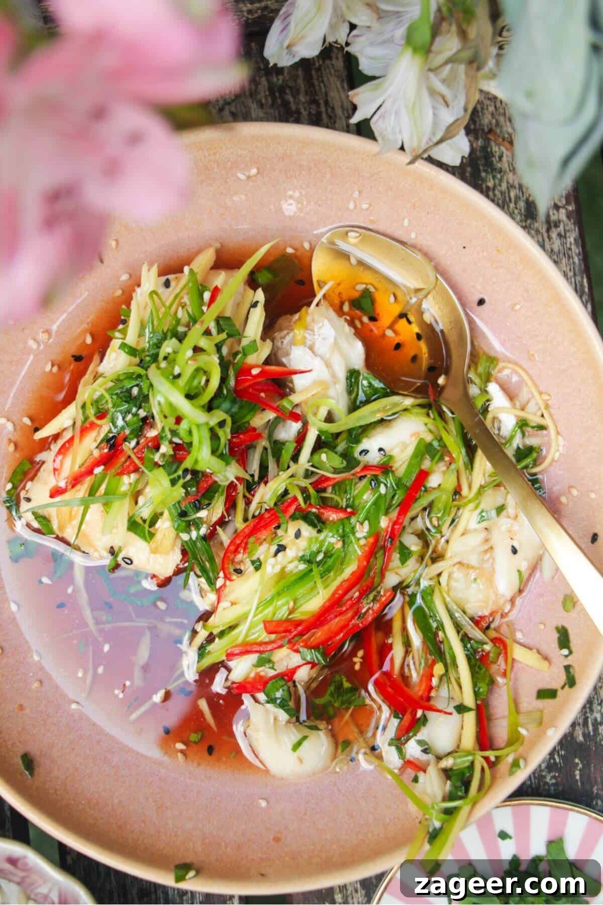 Aromatic Hot Oil Steamed Fish 2 Two succulent fish fillets topped generously with fresh scallions, thinly sliced ginger, and vibrant red chili in an elegant pink serving bowl, ready to be drizzled with sizzling oil.