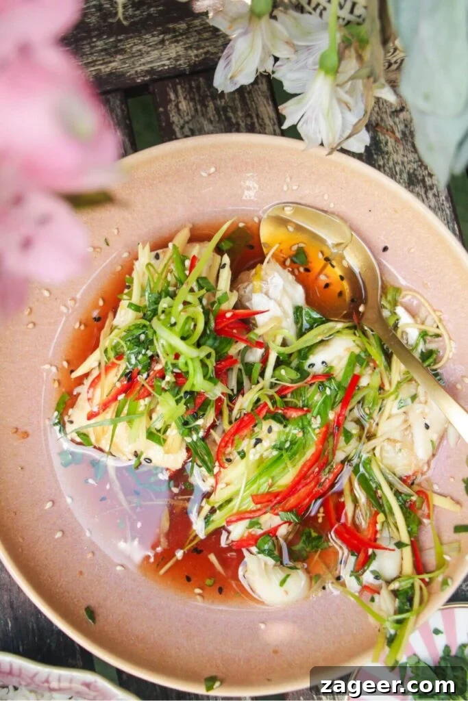 Aromatic Hot Oil Steamed Fish 11 A close-up shot of two glistening fish fillets, richly topped with bright green scallions, golden ginger, and red chili in a pink serving bowl, showcasing the final presentation.