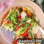 Two fish fillets topped with scallions, ginger and chili in a pink bowl.
