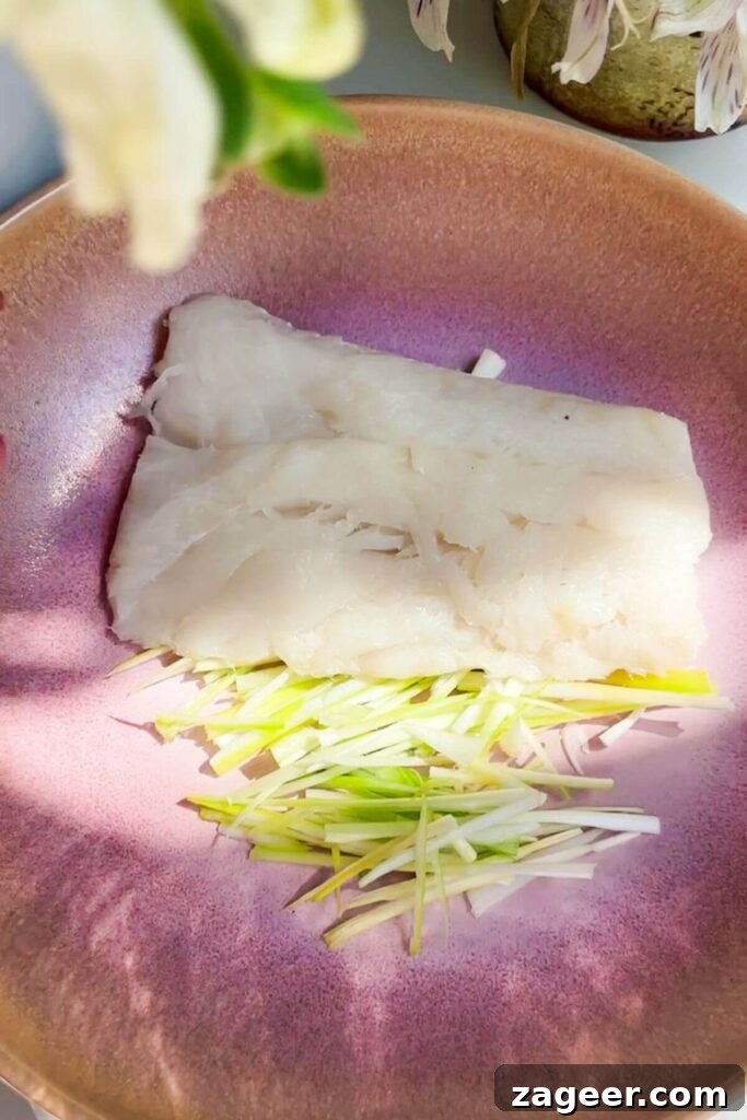 Aromatic Hot Oil Steamed Fish 4 A single piece of white fish fillet resting on a bed of thinly sliced white scallion parts in a charming pink heatproof bowl, seasoned lightly with salt.