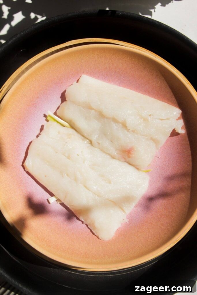 Aromatic Hot Oil Steamed Fish 6 Two pristine fish fillets, seasoned and arranged in a pink heatproof bowl, neatly placed within a steamer basket, ready for cooking.