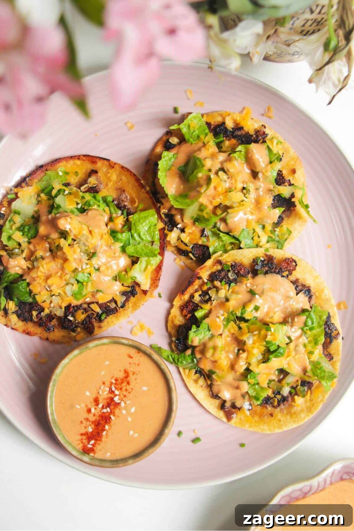 Smashed Cheeseburger Tacos 2 Three golden brown cheeseburger smash tacos piled high with fresh toppings and burger sauce, served on a vibrant pink plate, hinting at a delicious, easy meal.