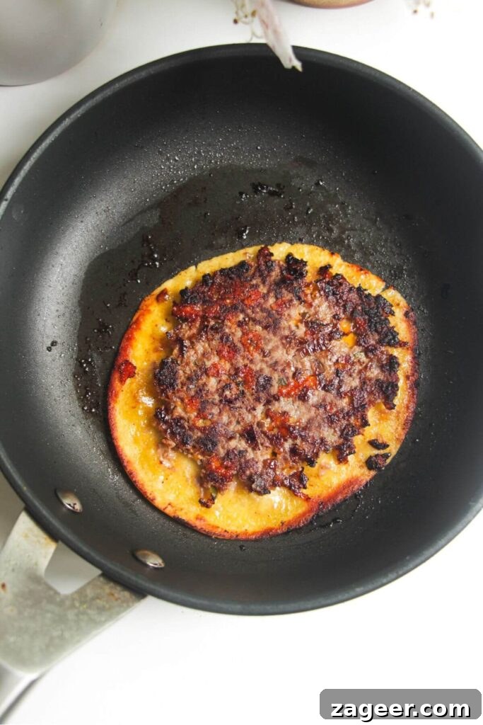 Smashed Cheeseburger Tacos 7 A single cheeseburger taco cooking in a small pan, meat-side down, demonstrating the smashing process.