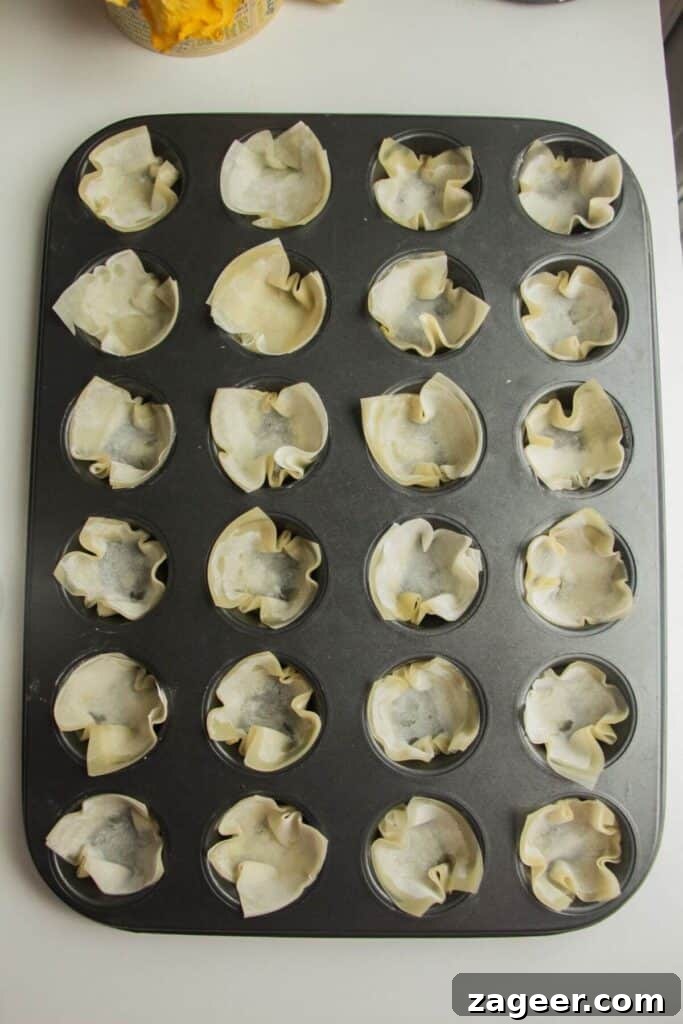 Sweet and Savory Bacon Gruyère Phyllo Tartlets 4 Filo pastry squares being pressed into a mini muffin tin to form cups.