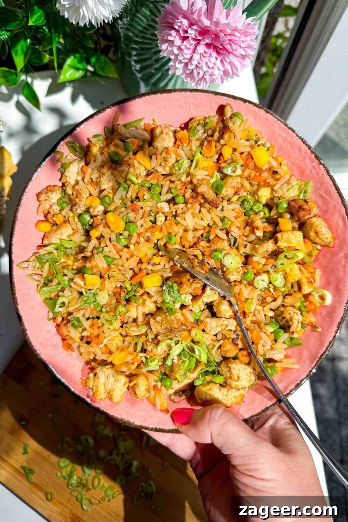 Effortless Air Fryer Chicken Fried Rice 2 Hand holding a vibrant pink bowl filled with golden-brown chicken fried rice, garnished with fresh green onions.