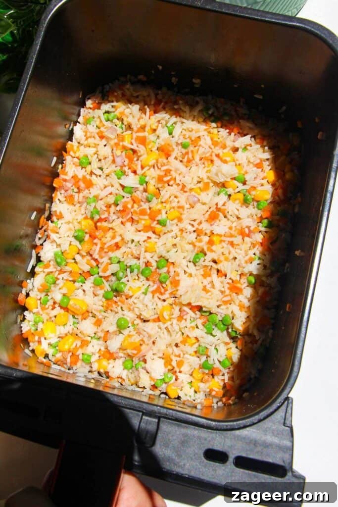 Effortless Air Fryer Chicken Fried Rice 5 Cooked rice, finely diced vegetables (onion, carrot), ginger, garlic, frozen peas, and corn mixed with all the sauces and seasonings in an air fryer basket.