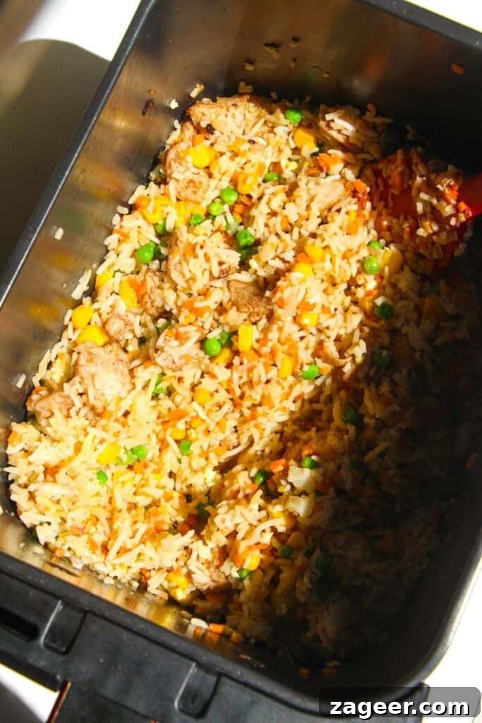 Effortless Air Fryer Chicken Fried Rice 7 Partially cooked chicken fried rice in the air fryer basket after the first round of cooking and stirring, showing browning edges.