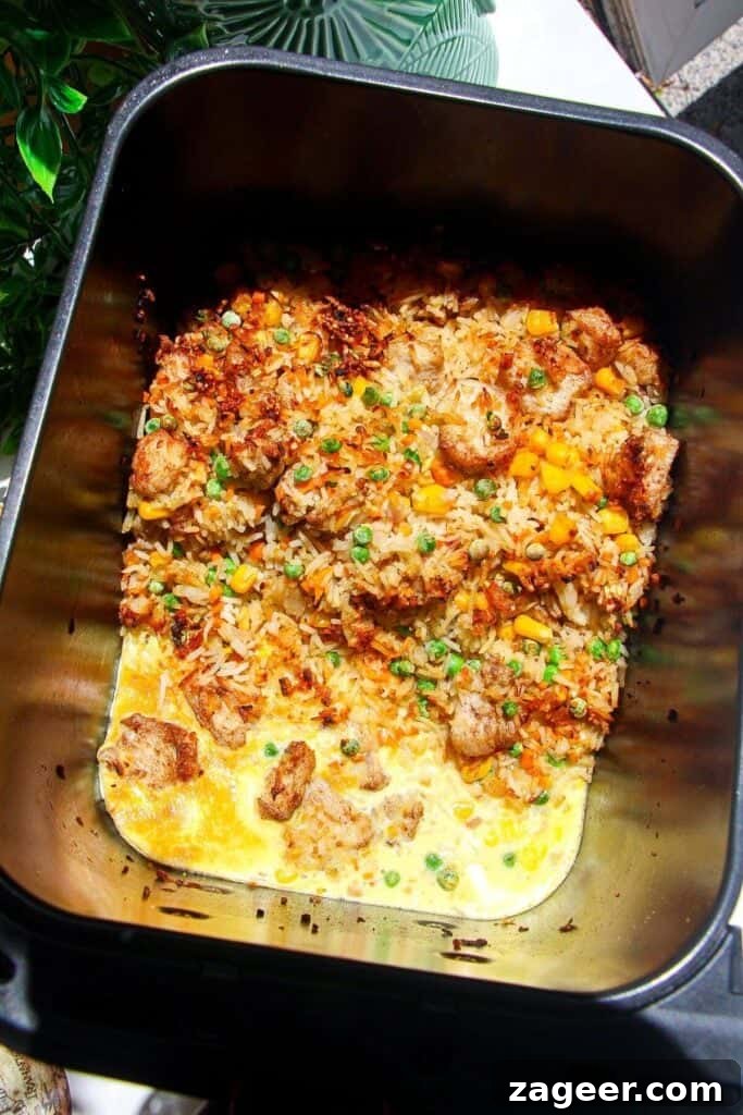 Effortless Air Fryer Chicken Fried Rice 8 Whisked egg poured into an empty space in the air fryer basket next to the cooking fried rice, ready to scramble.