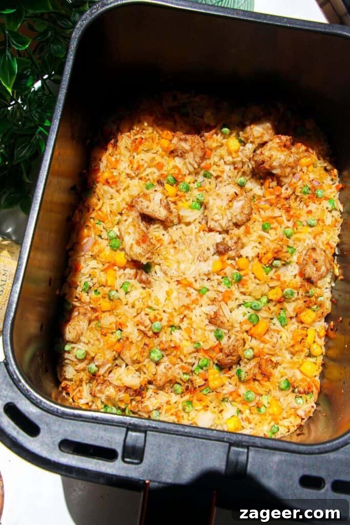 Effortless Air Fryer Chicken Fried Rice 9 Freshly cooked air fryer chicken fried rice, with scrambled eggs mixed in and garnished with green onions, still in the air fryer basket.