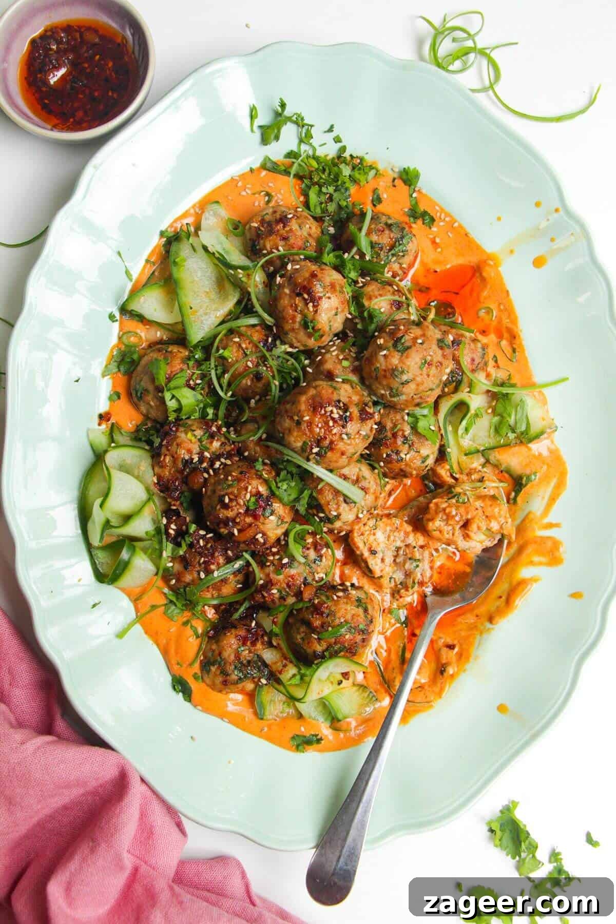 Creamy Gochujang Dumpling Meatballs 2 Dumpling meatballs on gochujang sauce with pickled cucumber on an oval platter.