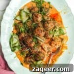 Dumpling meatballs on gochujang sauce with pickled cucumber on an oval platter.