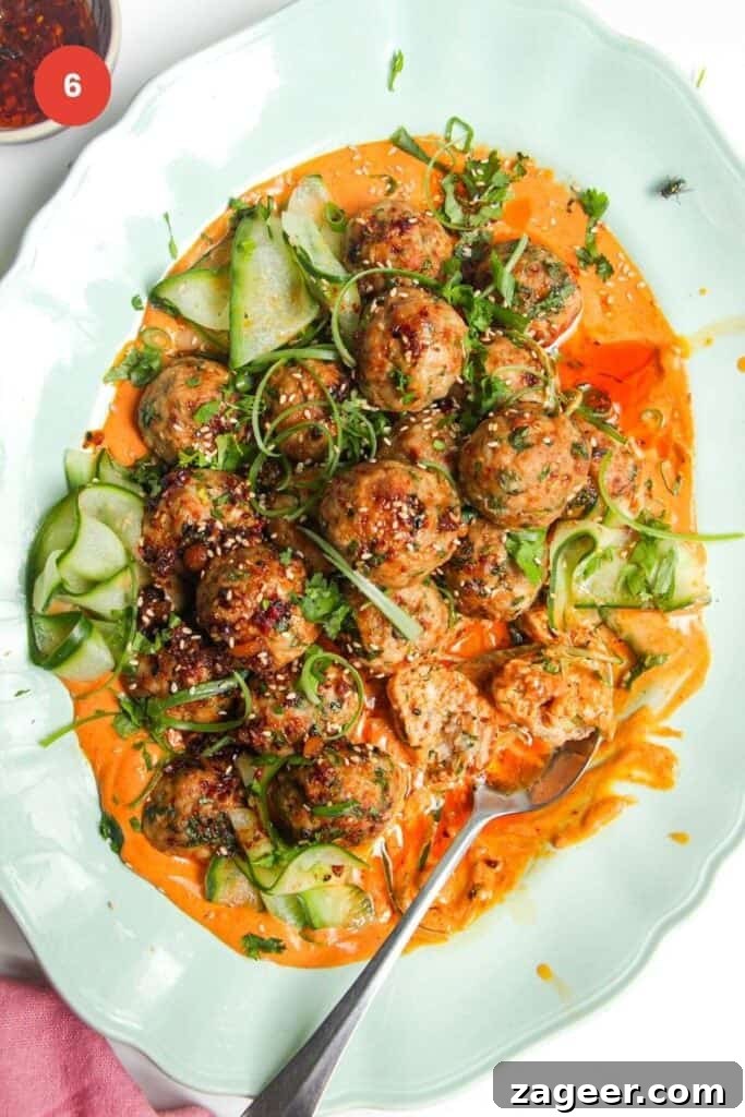 Creamy Gochujang Dumpling Meatballs 9 Dumpling meatballs on gochujang sauce with pickled cucumber on an oval platter.