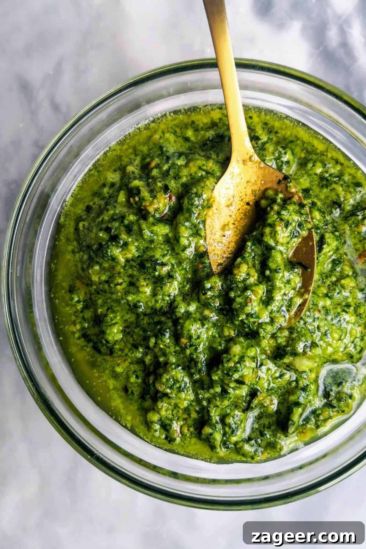 Homemade Basil Pesto So Good So Fast 2 Basil pesto in a small glass bowl, with a gold spoon on a grey marble background.