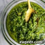 Basil pesto in a small glass bowl, with a gold spoon on a grey marble background.
