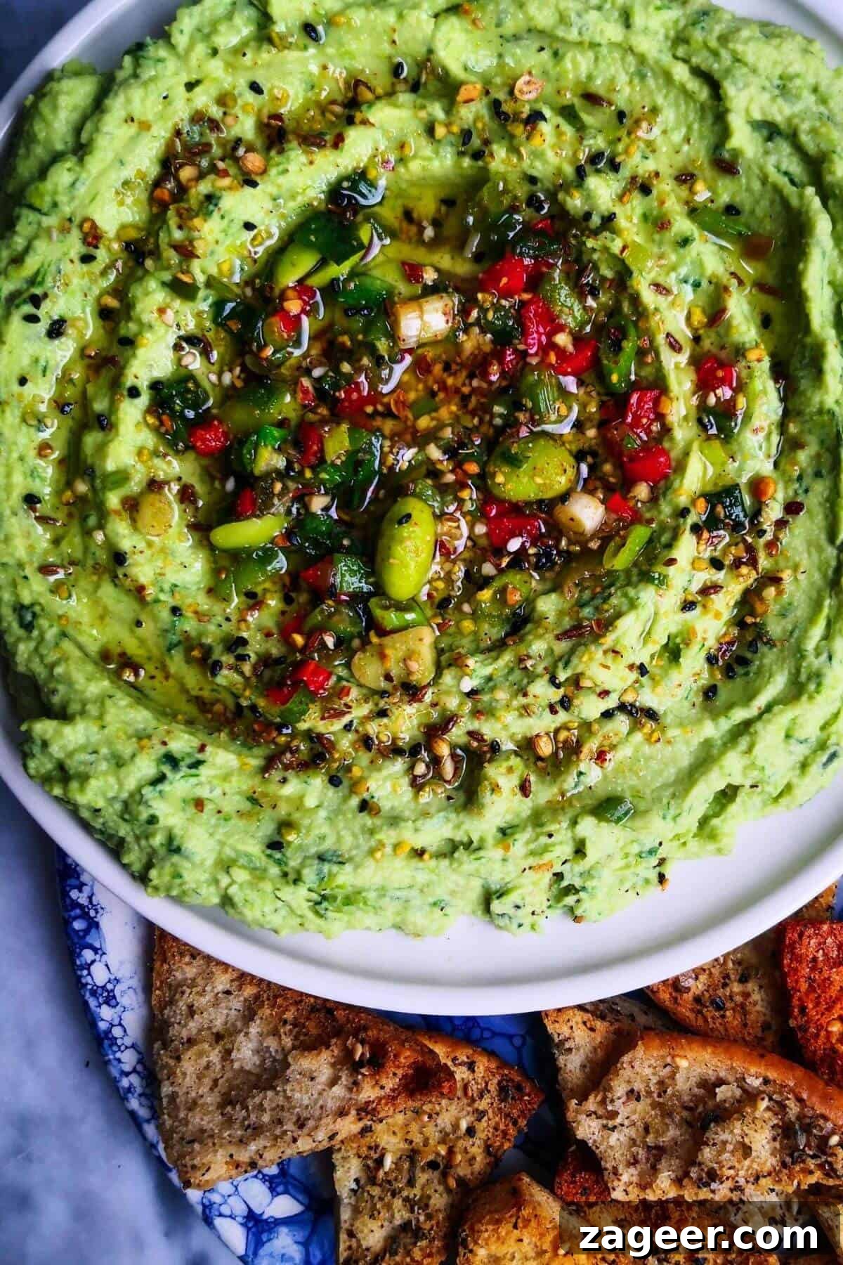 Vibrant Edamame Avocado Hummus 2 Edamame hummus with avocado on a small white plate, with pita chips on the side.